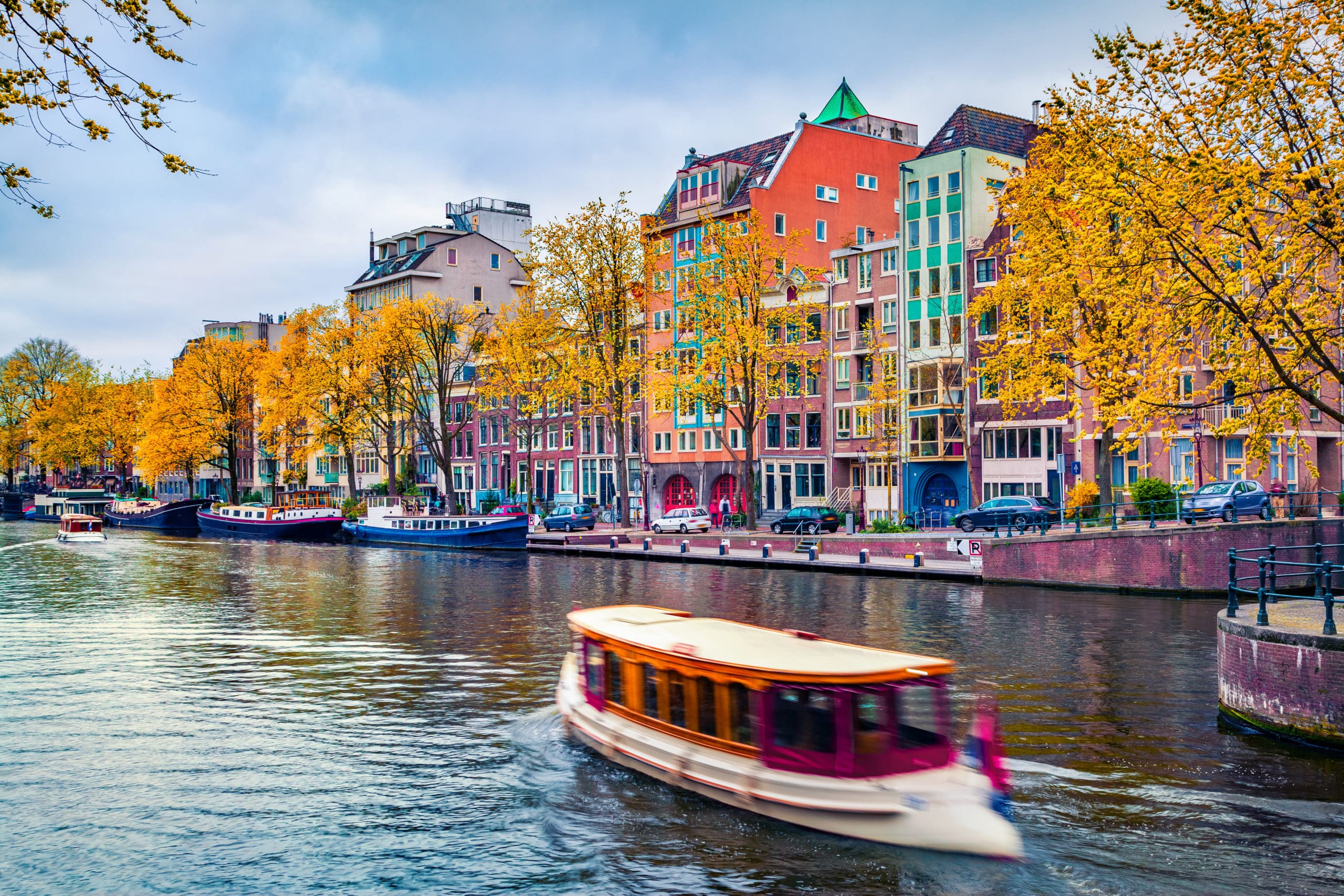 Picturesque autumn cityscape of Amsterdam. Splendid view of famous Dutch channels and excursion boat. Colorful morning landscape in Netherlands, Europe. Traveling concept background.